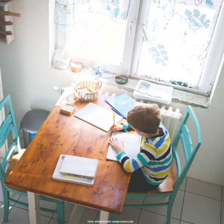 Ein Kind sitzt am Esstisch in der Küche und macht Hausaufgaben.